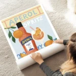 affiche aperol spritz illustree avec bouteille verre et oranges sur fond bleu ty au sol.webp
