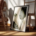 affiche avec de grandes feuilles de bananier vert fonce et blanc casse sur un fo encadre.webp