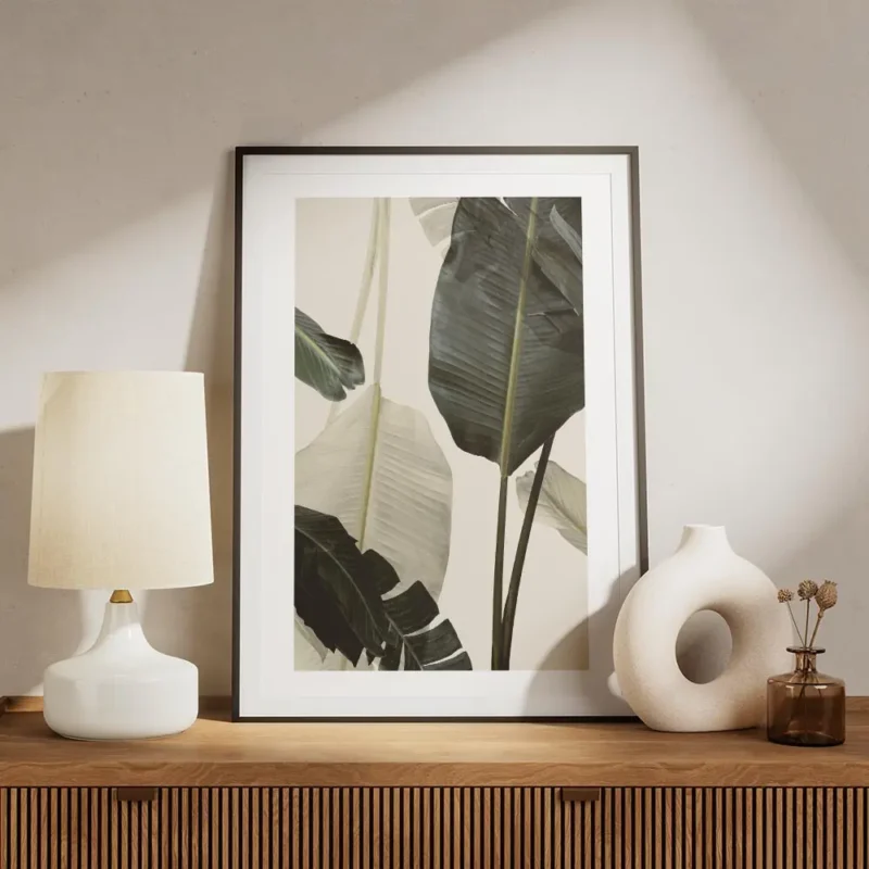 affiche avec de grandes feuilles de bananier vert fonce et blanc casse sur un fo meuble.webp