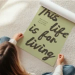 affiche avec les mots this life is for living en marron sur fond vert pale et un en rouleau.webp