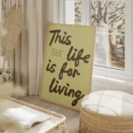 affiche avec les mots this life is for living en marron sur fond vert pale et un salon beige.webp