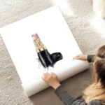 affiche avec un rouge a levres chanel rose pale et dore sur fond blanc avec une au sol.webp