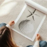 affiche avec une etoile de mer et un coquillage blanc sur du sable pale en rouleau.webp