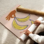 affiche avec une main orange tenant des bananes jaunes et bleues sur fond rose p enroule.webp