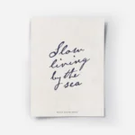 affiche beige avec le texte manuscrit slow living by the sea en bleu fonce et fe.webp