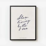 affiche beige avec le texte manuscrit slow living by the sea en bleu fonce et fe avec cadre.webp