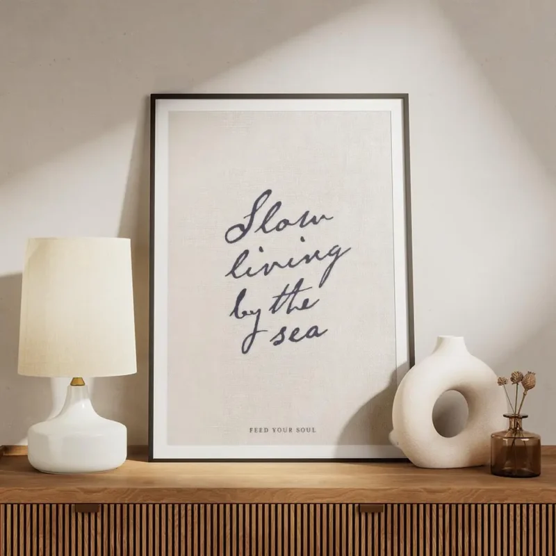 affiche beige avec le texte manuscrit slow living by the sea en bleu fonce et fe meuble.webp