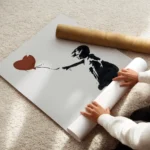 affiche de banksy fillette en noir tendant la main vers un ballon coeur rouge su enroule.webp