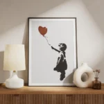 affiche de banksy fillette en noir tendant la main vers un ballon coeur rouge su meuble.webp