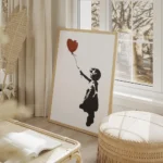 affiche de banksy fillette en noir tendant la main vers un ballon coeur rouge su salon beige.webp