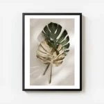 affiche de feuilles de monstera une verte et une doree posees sur un fond clair avec cadre.webp