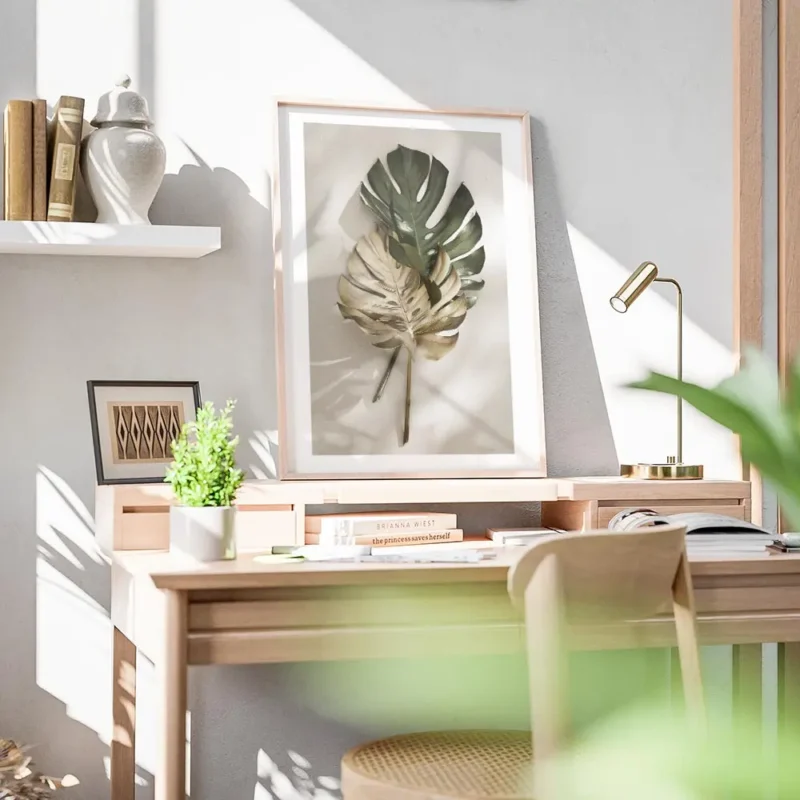 affiche de feuilles de monstera une verte et une doree posees sur un fond clair bureau.webp