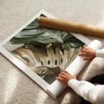 affiche de feuilles de monstera une verte et une doree sur un fond beige avec un enroule.webp