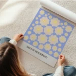 affiche de fleurs marguerite jaune souriantes sur fond bleu avec le texte the da en rouleau.webp